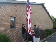 Staff members raise flag at outdoor flagpole.